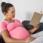 Vue côté de femme enceinte en train de lire sur le divan