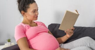 Vue côté de femme enceinte en train de lire sur le divan