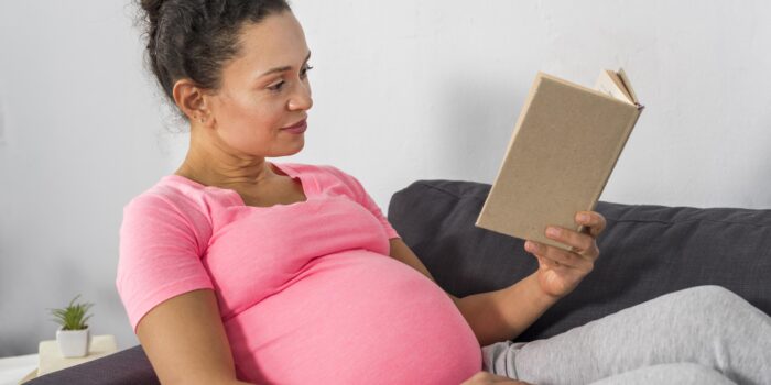 Vue côté de femme enceinte en train de lire sur le divan