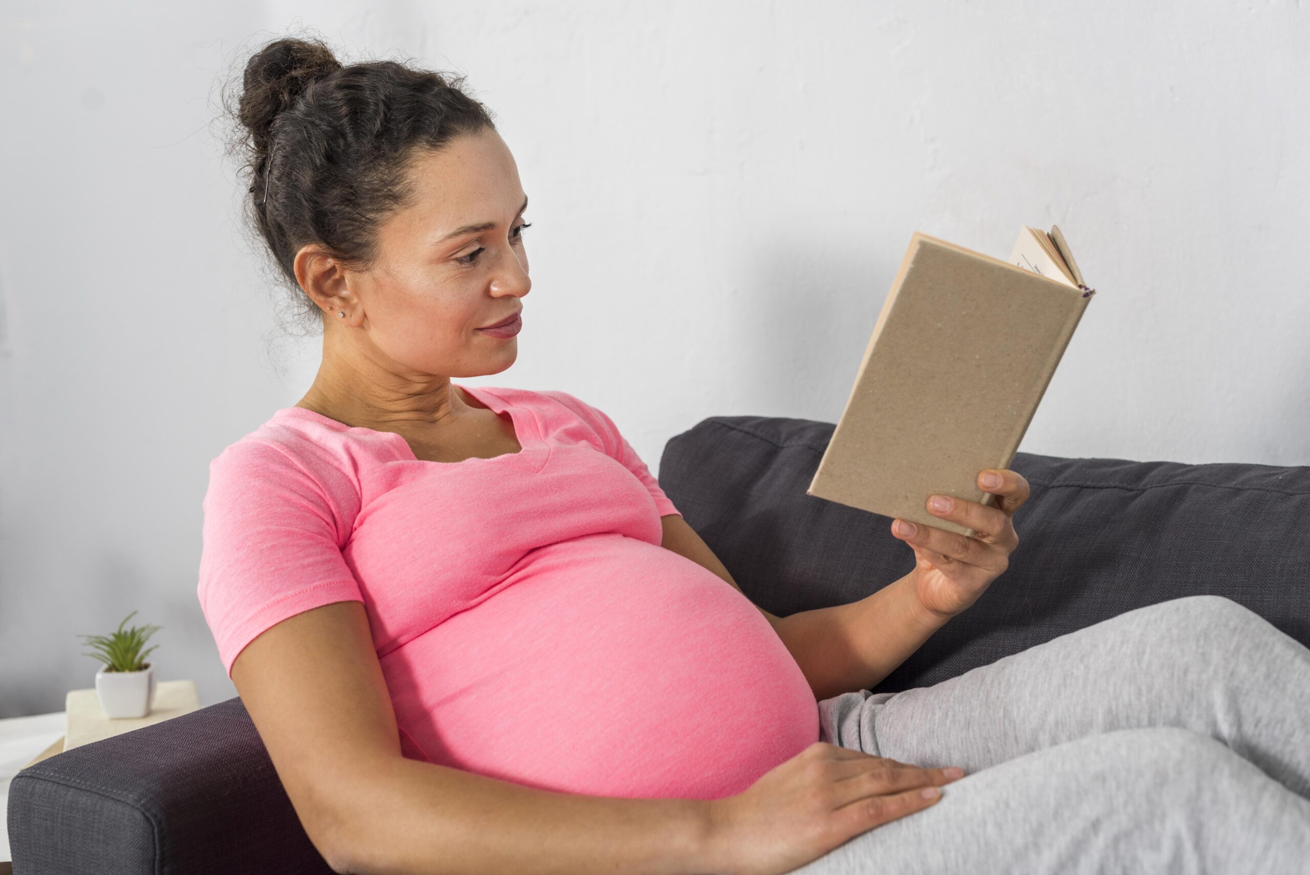 Vue côté de femme enceinte en train de lire sur le divan