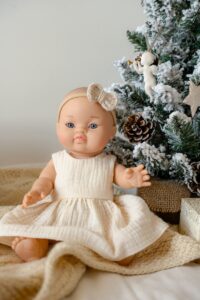 A doll sitting on a blanket next to a christmas tree